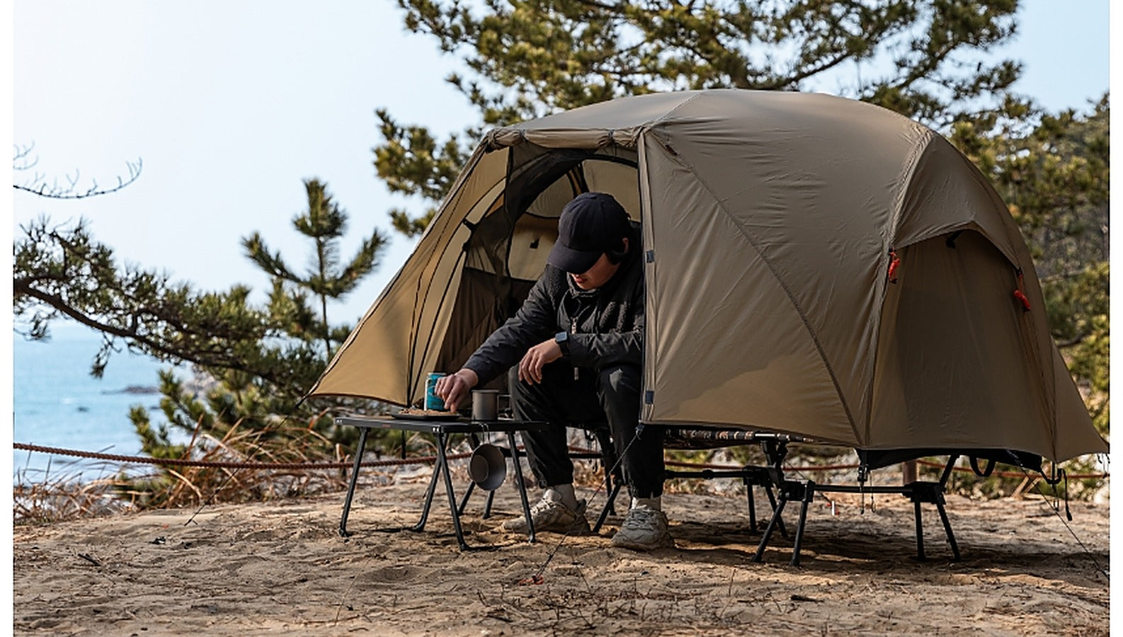 Camper cooking beside the pitched Base Cot Tent