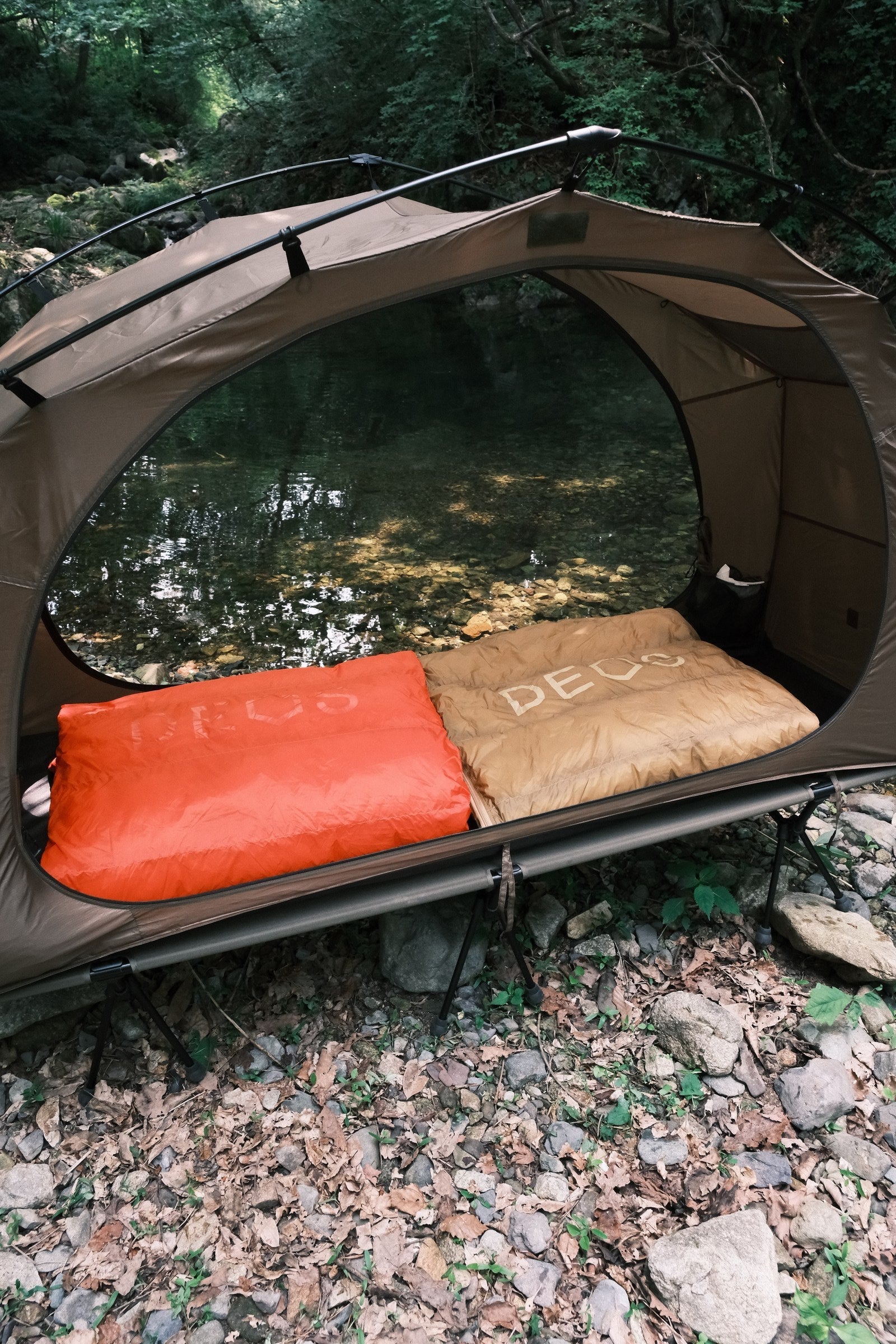 Orange and tan DEOS camp comforters spread side by side in a tent