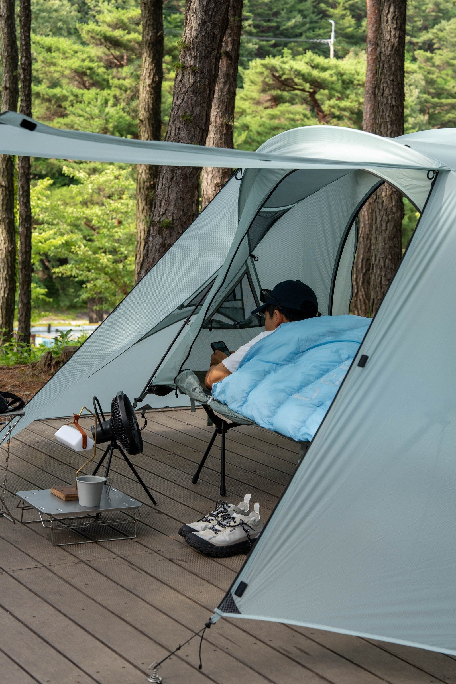 Camper relaxing inside a tent under a sky blue DEOS camp comforter