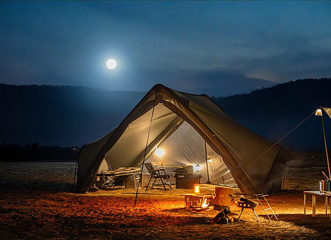 Super Position MGX-600 glowing at night under a full moon, camp chairs and fire pit set up on open ground