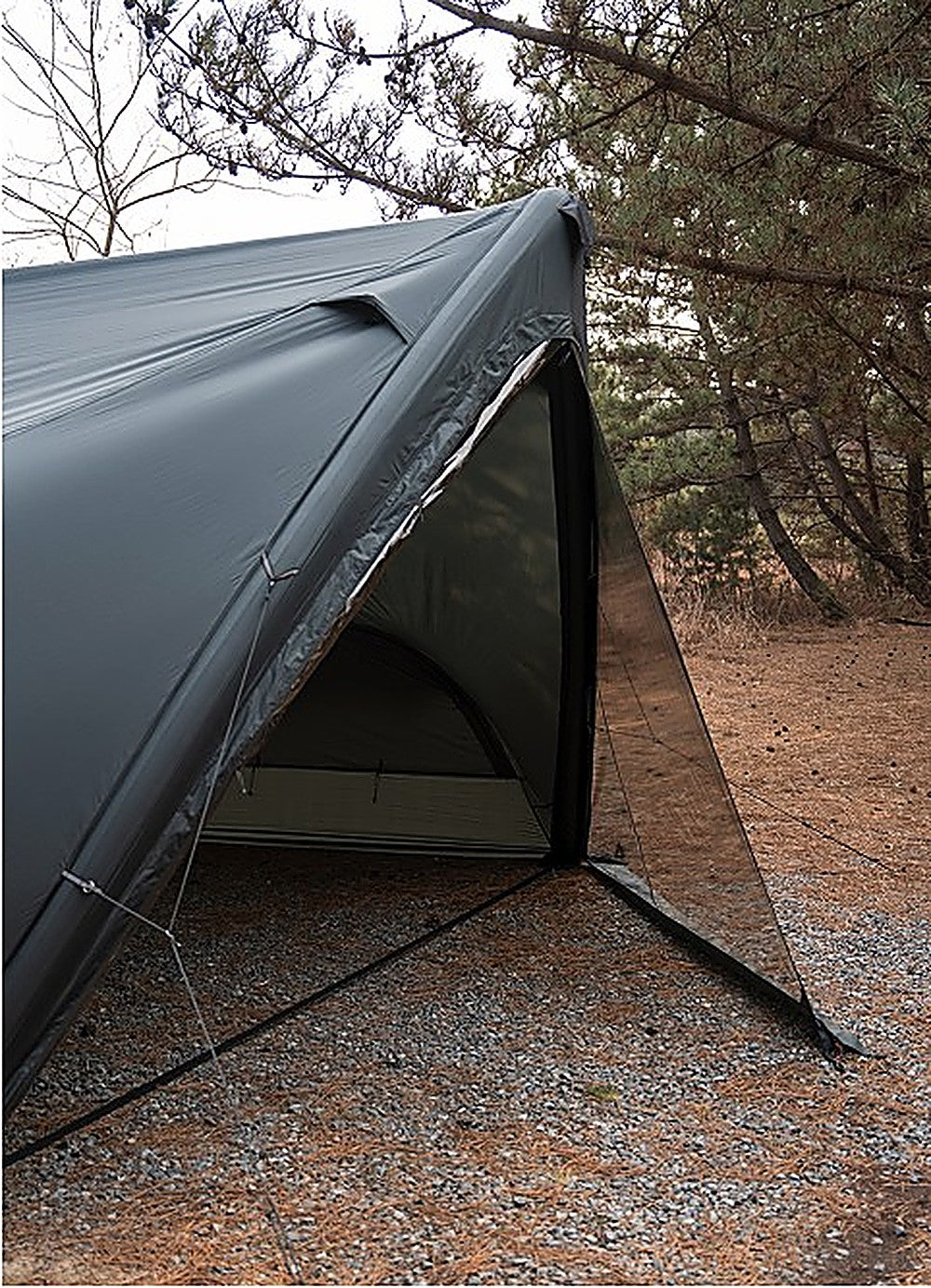Side detail of the MGX-600 TPU Door where the clear panel meets the charcoal fly, guyed out over gravel ground