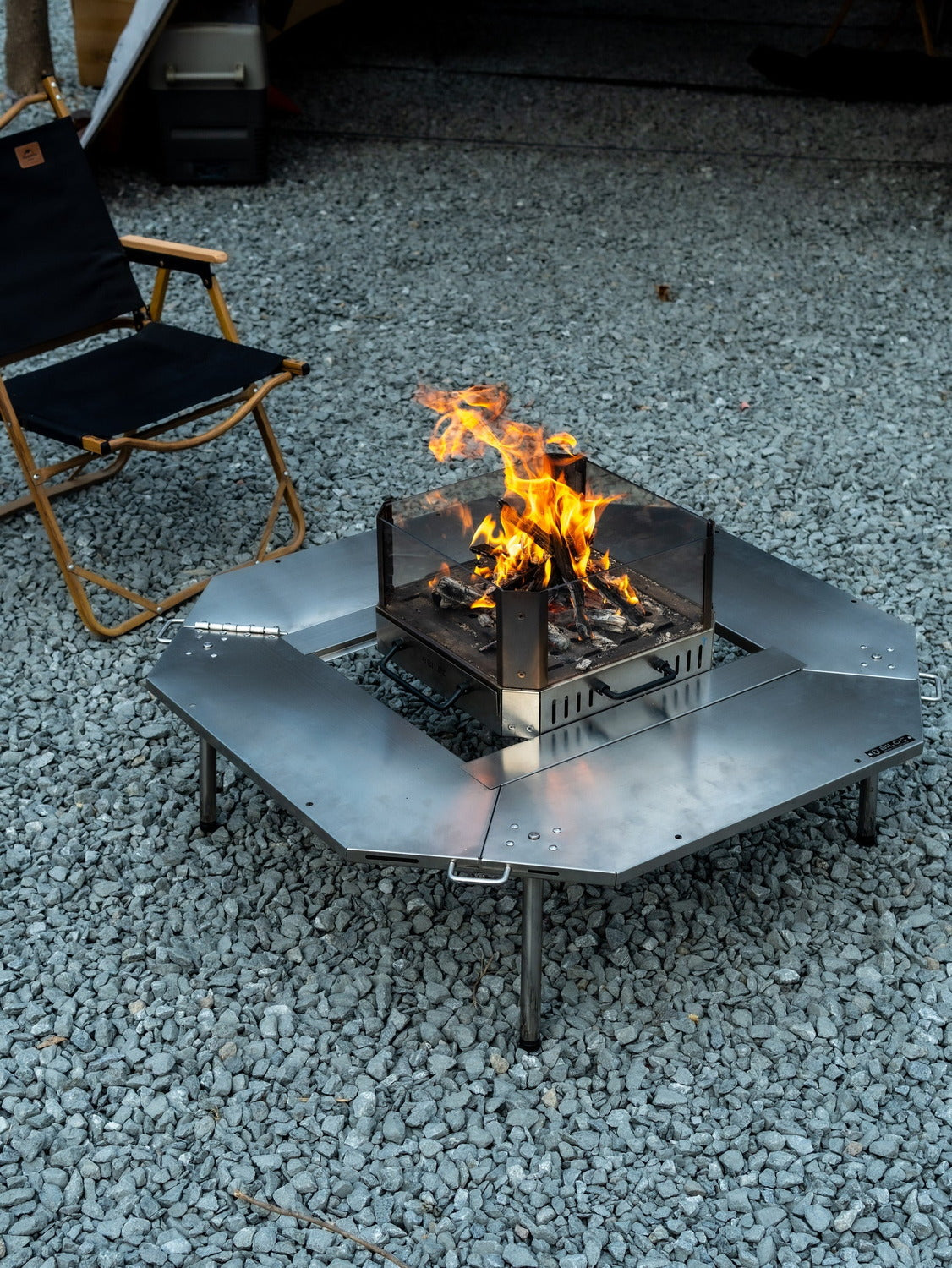 Biloc Octa table set up on gravel outdoors with a fire burning in a stove sitting in the centre opening. The stove is a separate purchase.