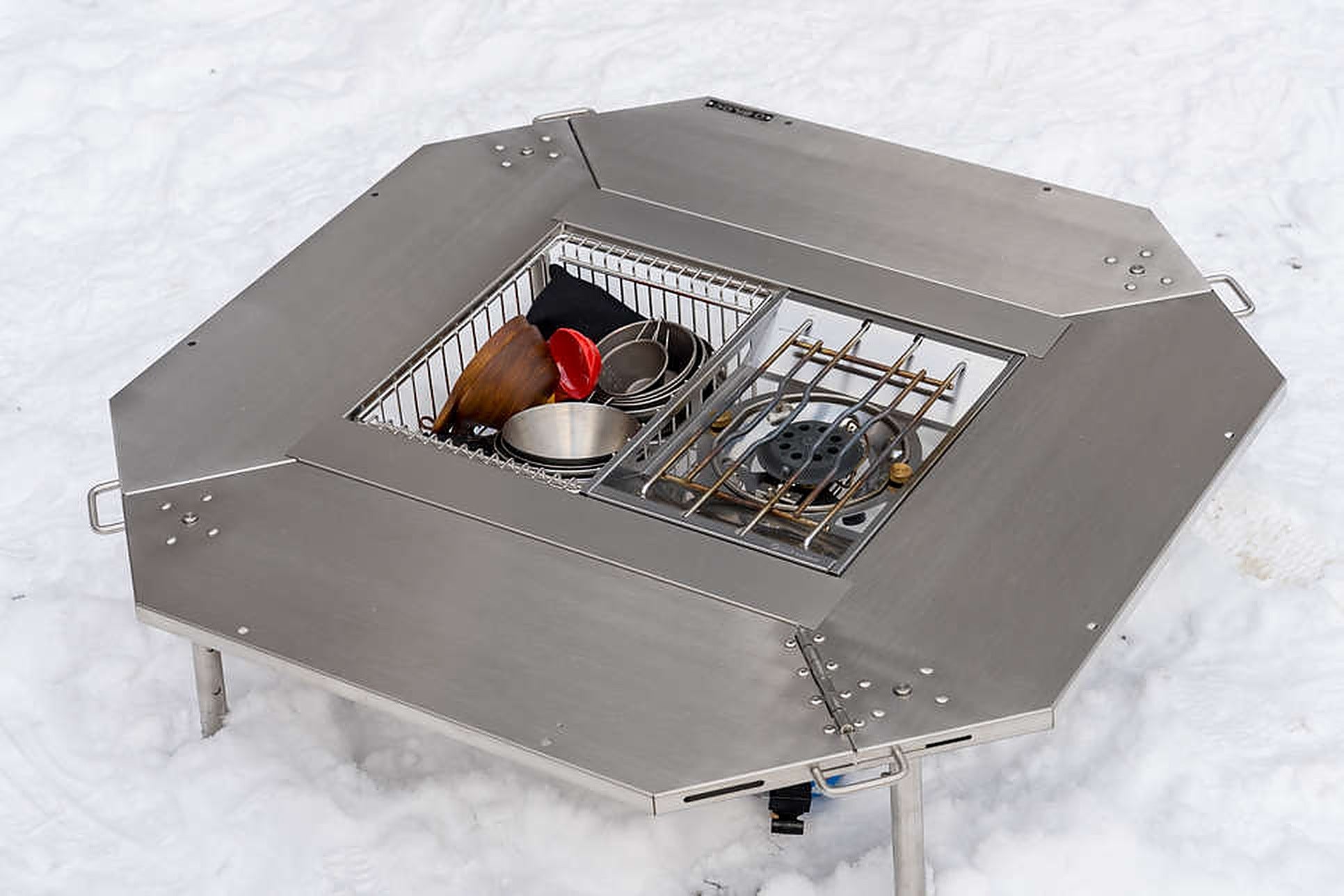 Top-down view of the Octa table with the inner table set fitted, holding an IGT burner in one unit of the centre bay and a wire storage basket in the other. The burner and basket shown are sold separately.