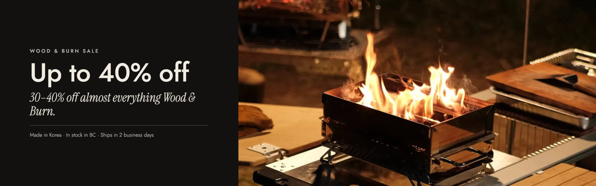 Wood & Burn Sale, up to 40% off: the Uniconn-M fire pit grill burning wood on a camp table at night, flames rising above the stainless body