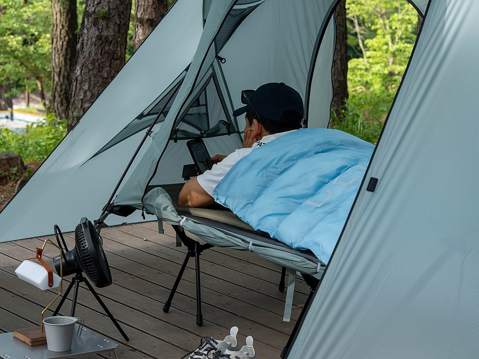 Camper tucked into a sky blue DEOS camp comforter on a cot inside a tent