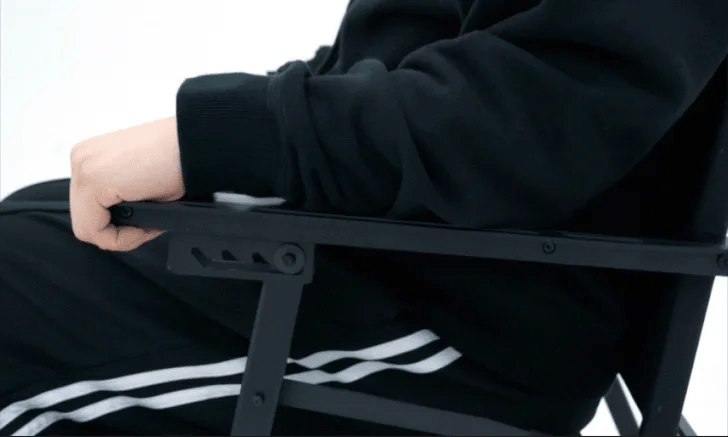 Hand lifting the FLOW folding chair armrest handle to adjust the backrest recline angle