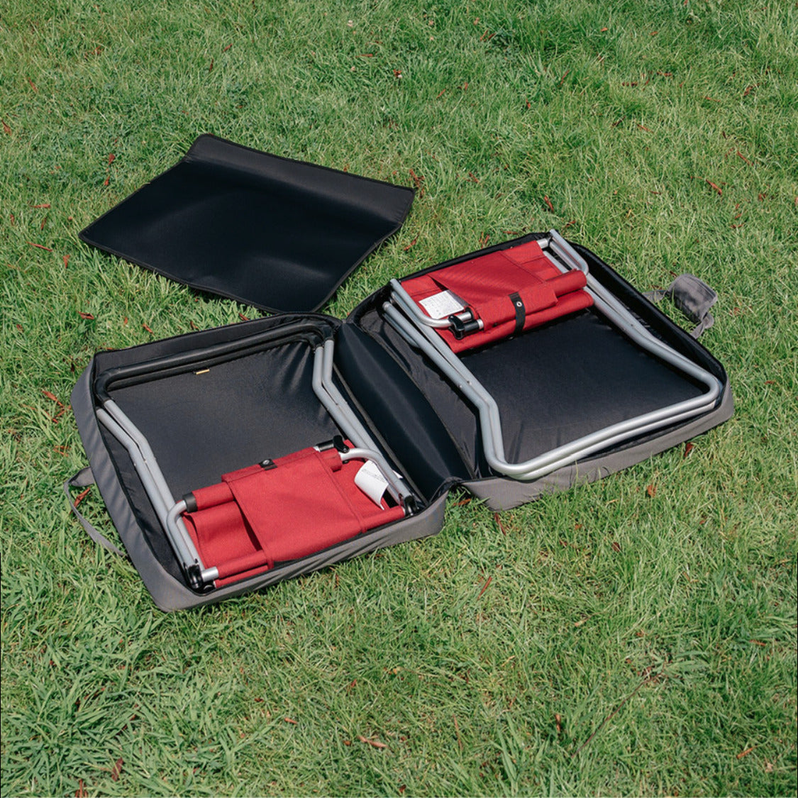 CORDURA FD Chair Case opened flat on grass with two folded red FD Chairs, one in each half