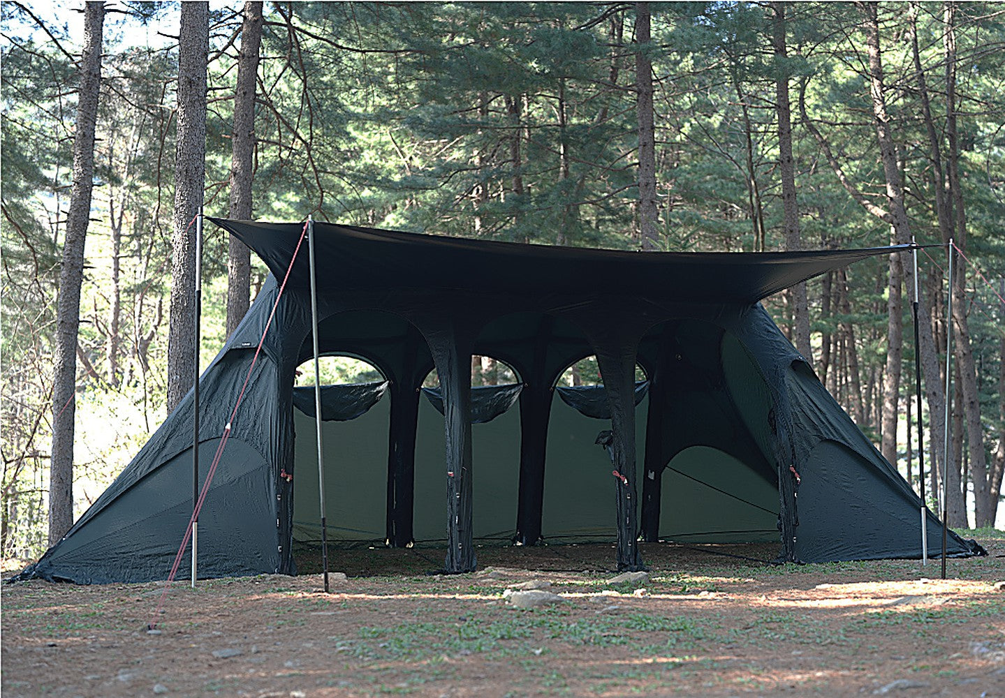 Front view of the shelter with the side tarp pitched taut overhead to shed rain over the seating area