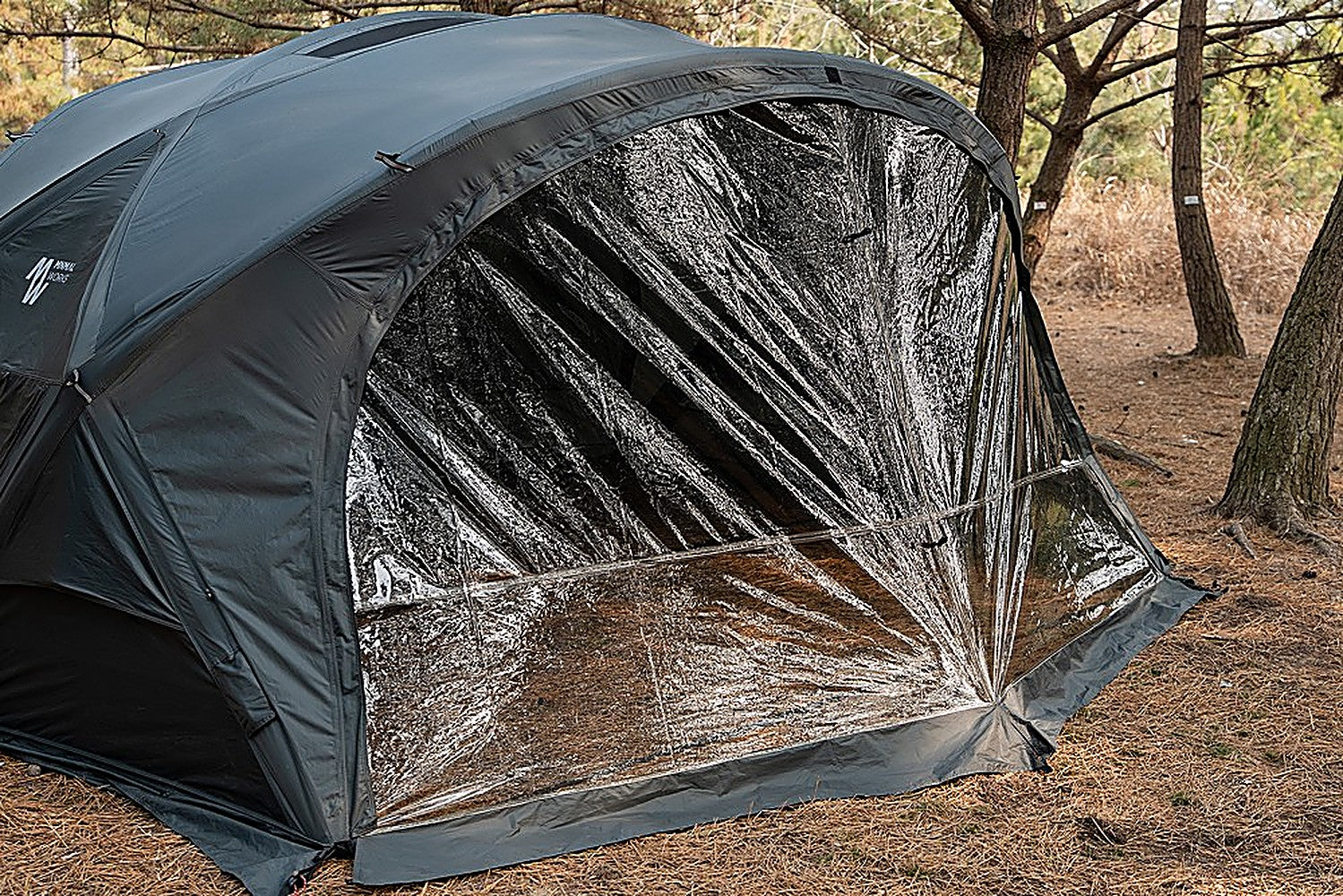 Angled close-up of the Shelter GM TPU Door film panel and edge zipper on the charcoal tent, pine-needle ground below