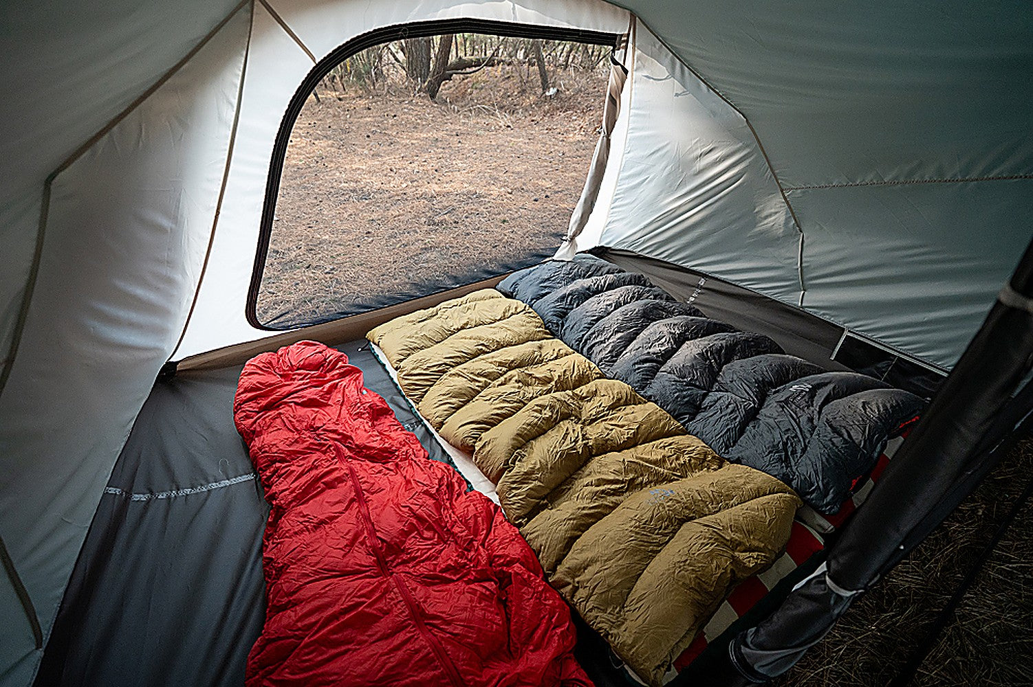 Three sleeping bags in red, tan and gray laid side by side across the full floor width of the inner tent