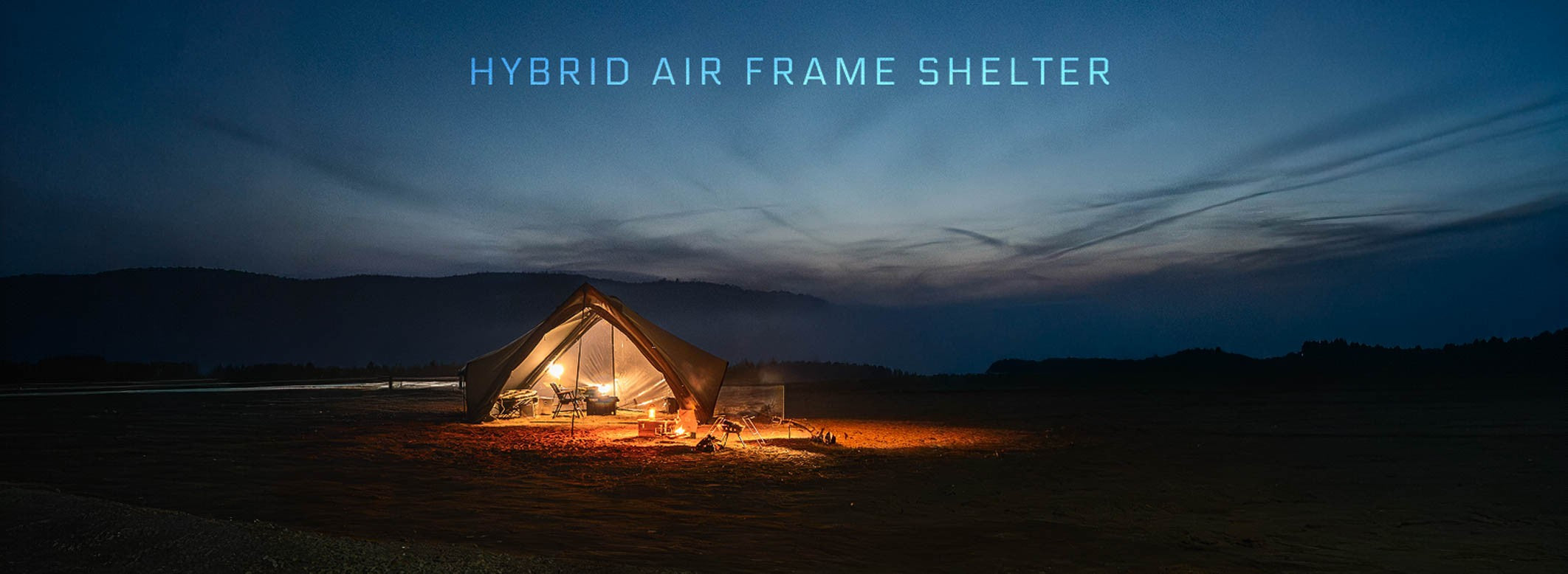 Minimal Works Super Position MGX-600 hybrid air-frame A-frame shelter lit at a riverside campsite at dusk