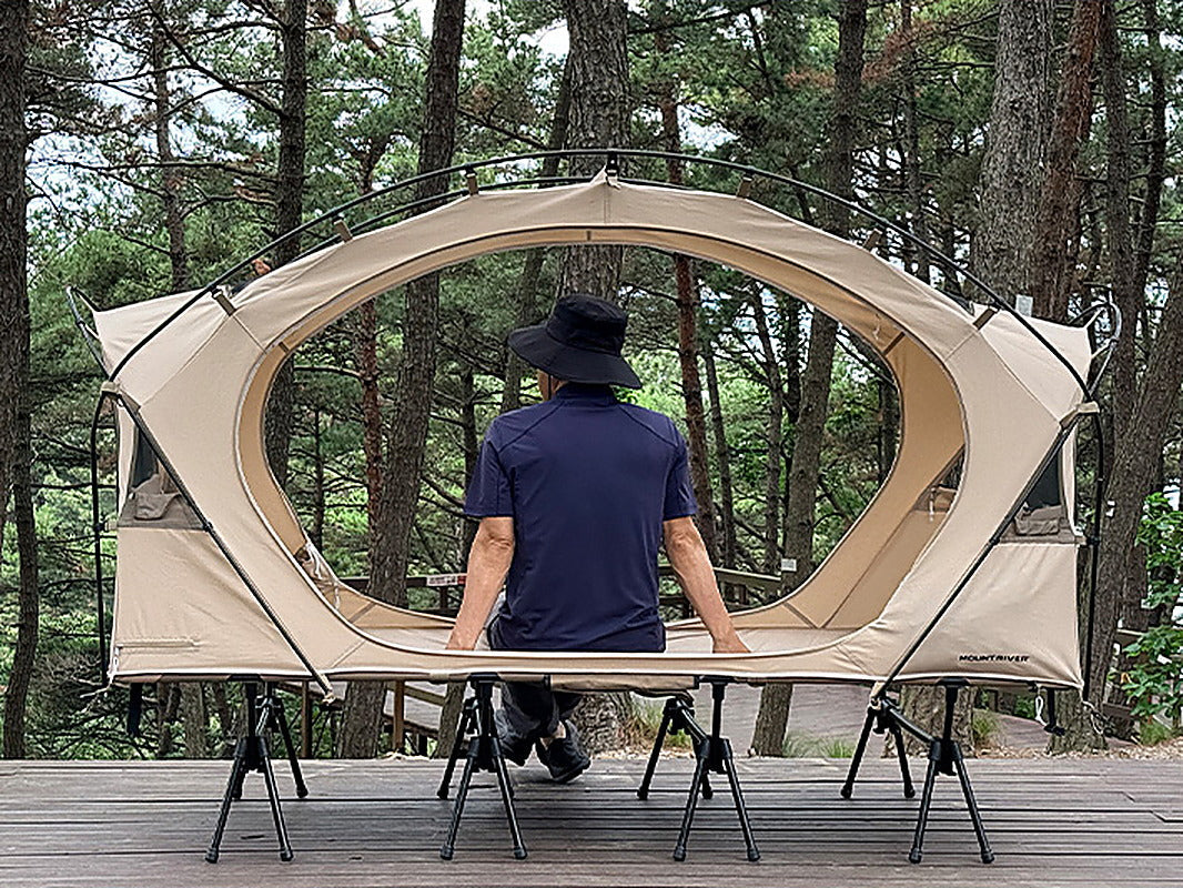 Camper sitting upright inside the Neo Nest 80 cot tent with head clearance above (cot sold separately).