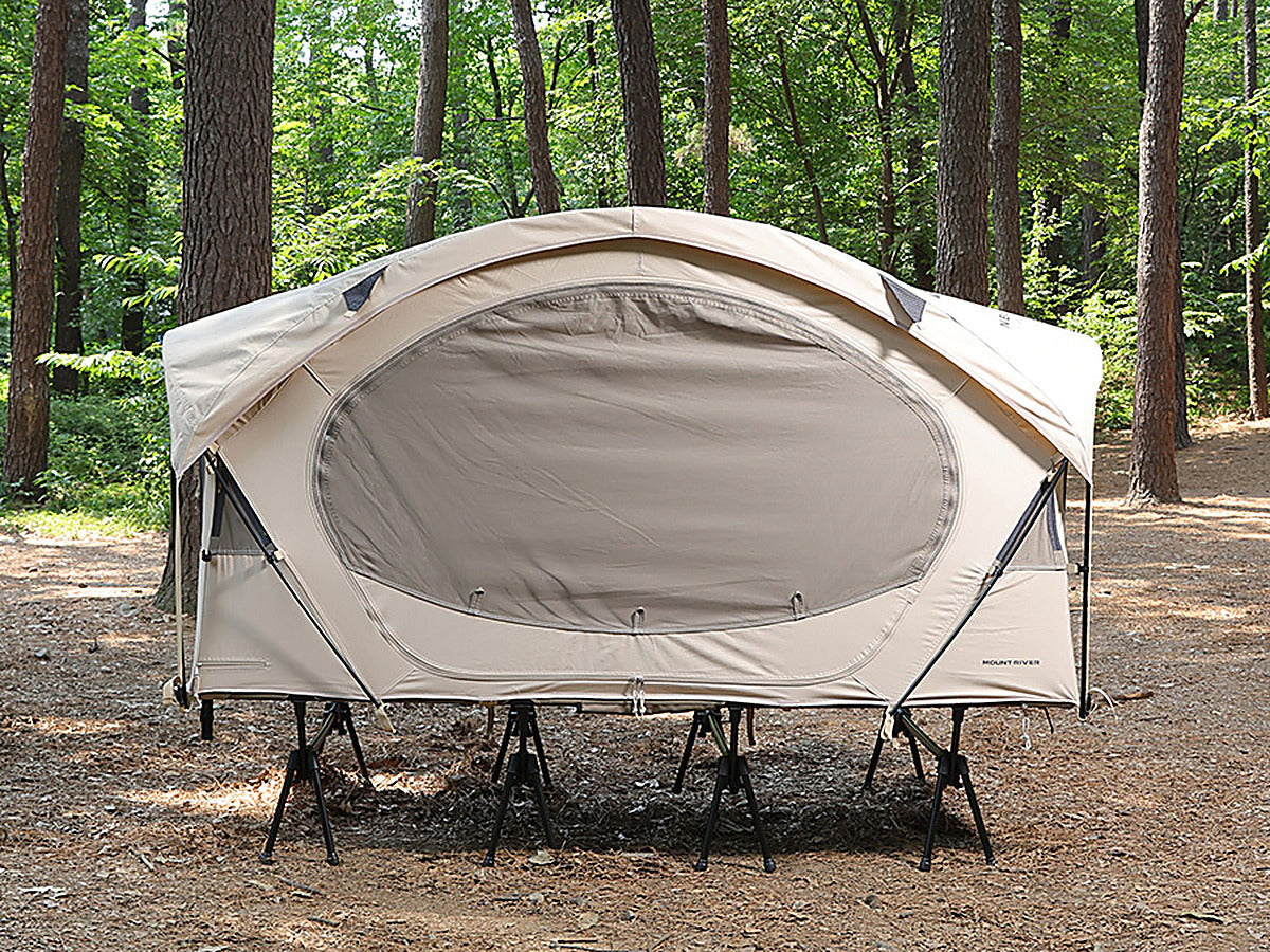 Neo Nest 80 cot tent pitched on a camp cot in a pine forest, side window closed (cot sold separately).