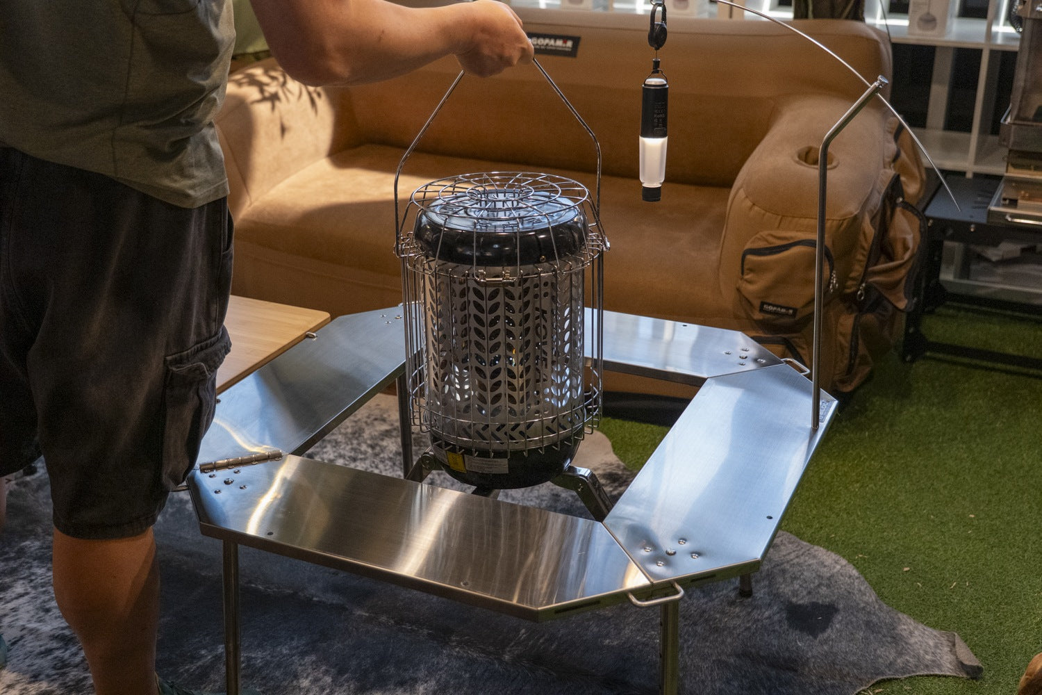 Caged gas heater being lifted by its bail handle into the open centre of the Biloc Octa table in a showroom. The heater, lantern and hanger shown are not included.