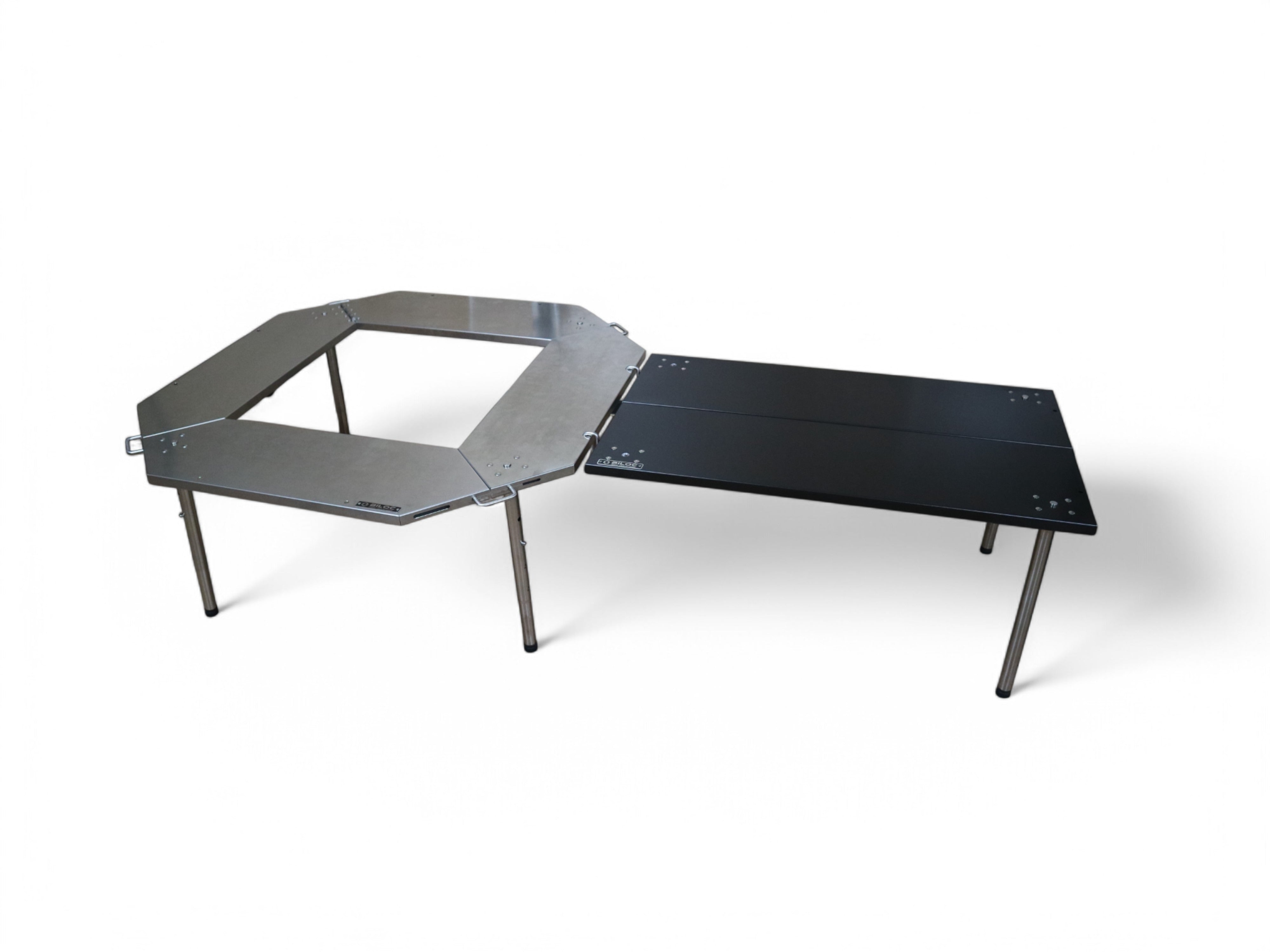 Black Ribera table joined as a side wing to a silver Biloc Octa fire ring table, both set to the same low working height.
