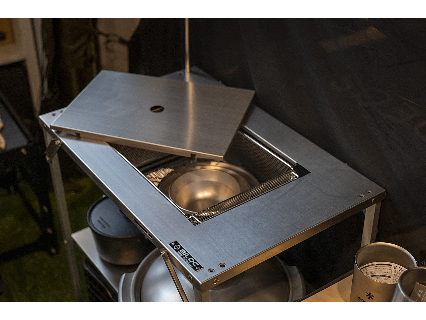 Stainless bowl and mesh basket unit dropped into the Stella shelf's top IGT bay, with the top plate slid half open. The inserts shown are not included.