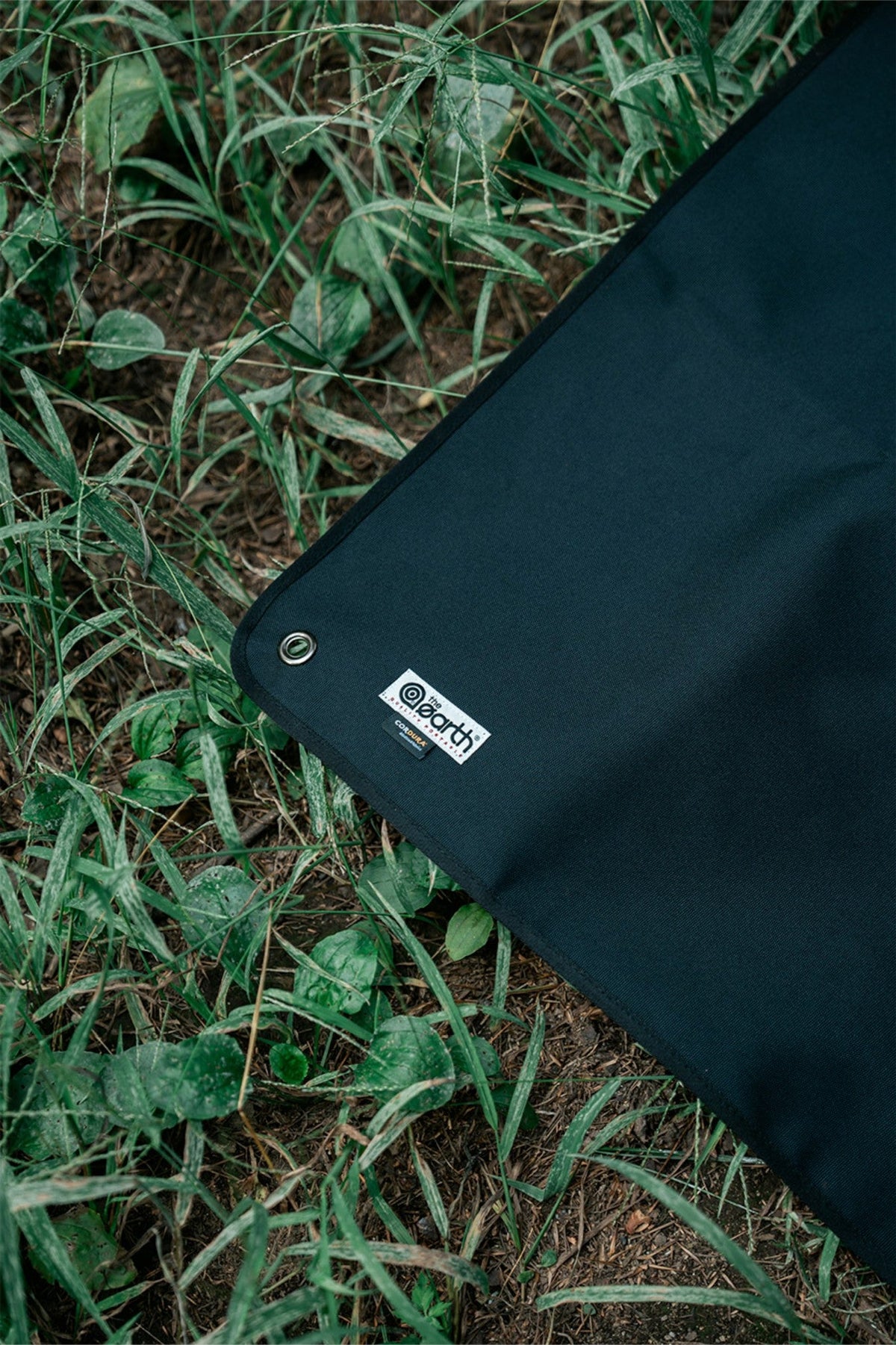 Corner of the Black sheet on grass, with the label and a metal eyelet
