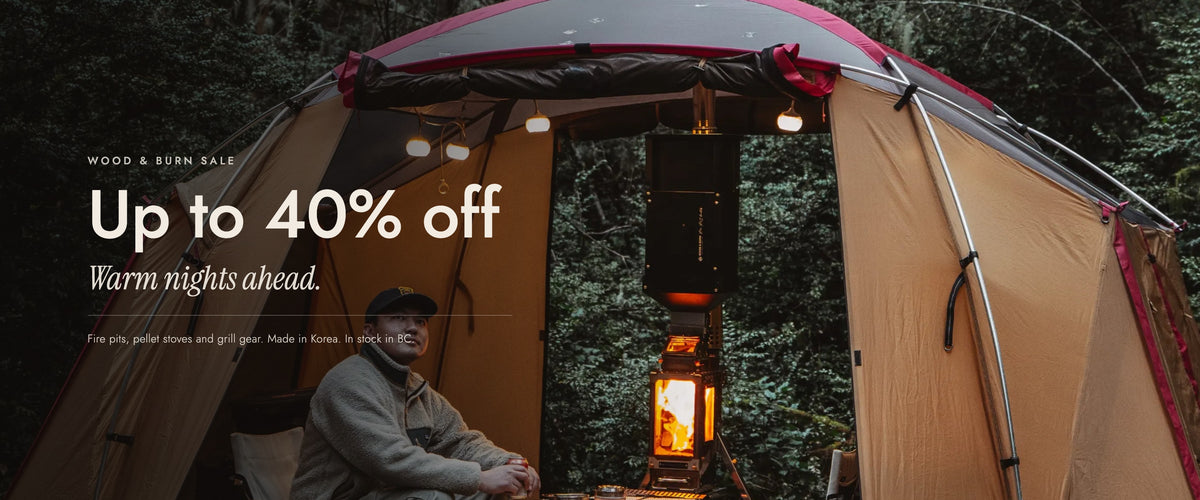 Wood & Burn Sale, up to 40% off. Warm nights ahead. Fire pits, pellet stoves and grill gear, made in Korea and in stock in BC. A camper sits in an open tent beside a lit stove.